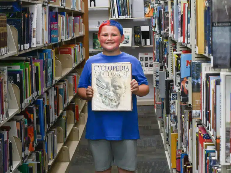 A smiling boy holds a non-fiction book in the Casey County Public Library